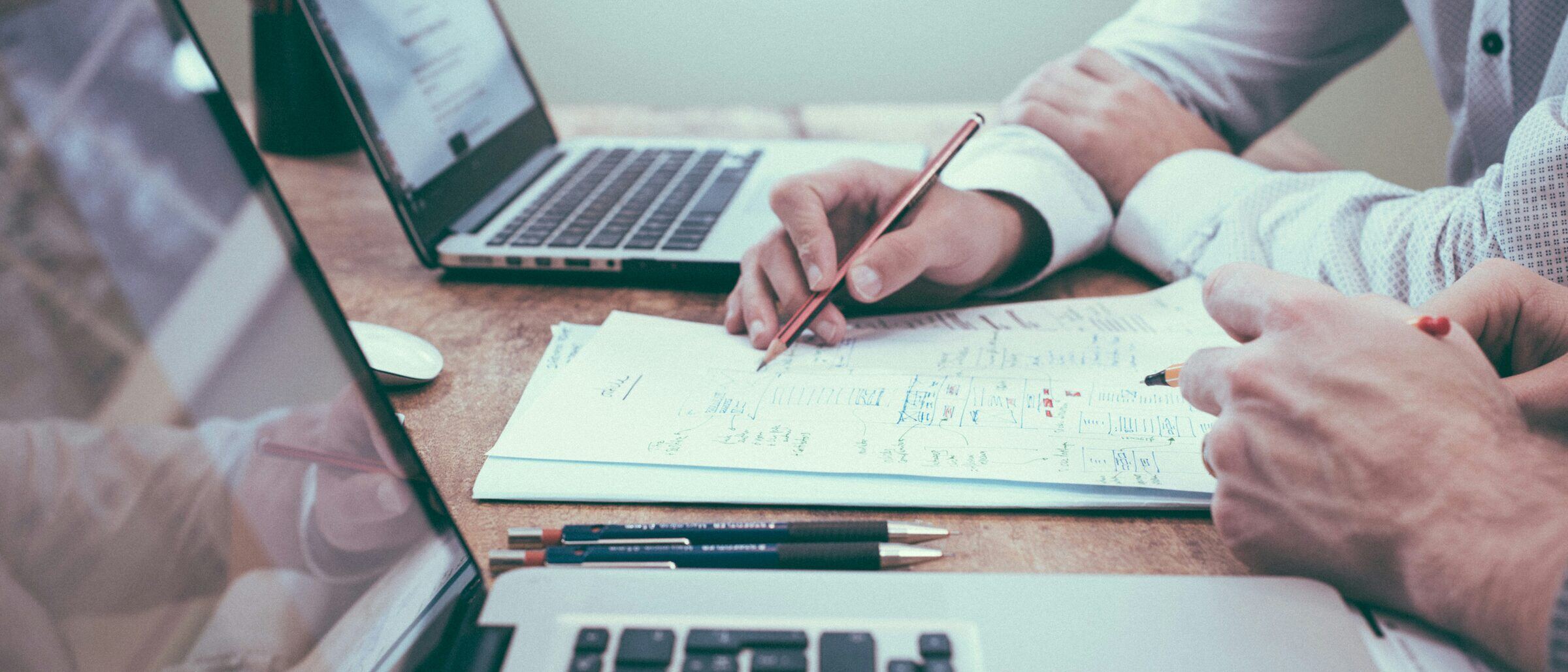 Two people at a table working out a diagram in a notebook, laptops beside them.